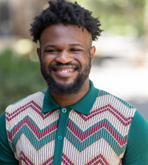 Smiling Black man with short afro and beard, wearing chevron knit sweater, outdoor portrait